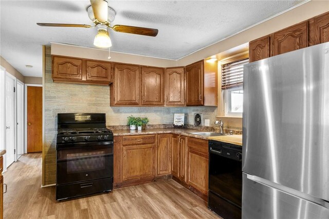 kitchen featuring light wood finished floors, decorative backsplash, brown cabinetry, black appliances, and a sink