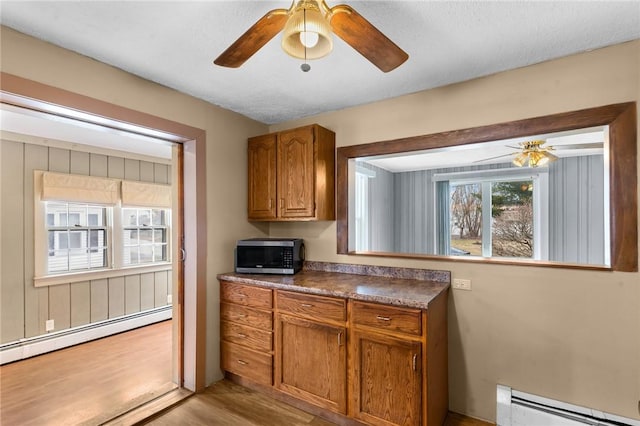 kitchen with brown cabinetry, a baseboard radiator, and stainless steel microwave