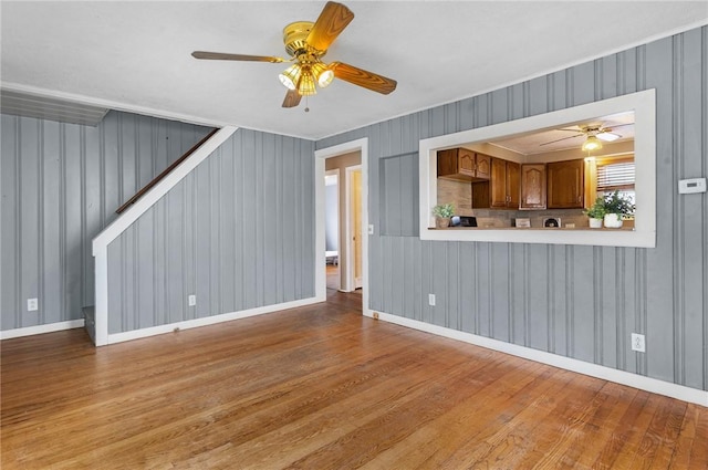 unfurnished living room with stairs, ceiling fan, baseboards, and wood finished floors