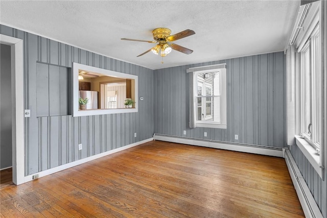 unfurnished room with a textured ceiling, hardwood / wood-style floors, a baseboard radiator, and a ceiling fan