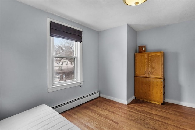 bedroom featuring a baseboard heating unit, baseboards, and light wood-style floors