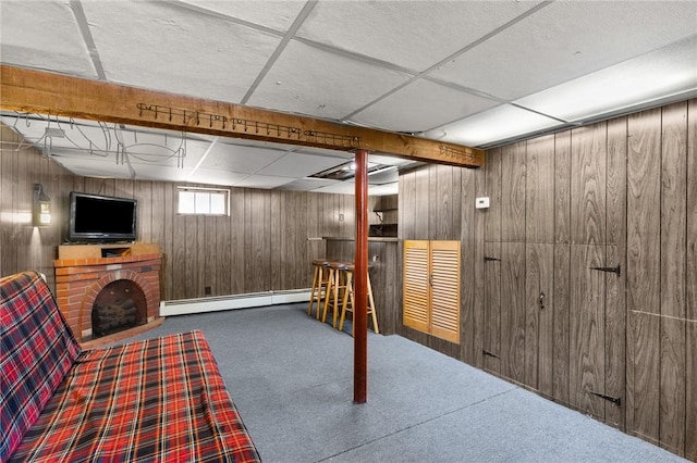 below grade area featuring a paneled ceiling, baseboard heating, a brick fireplace, carpet flooring, and wood walls