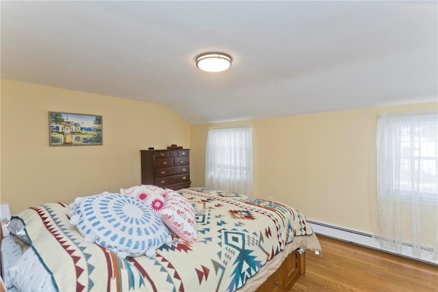 bedroom featuring lofted ceiling, a baseboard heating unit, multiple windows, and wood finished floors