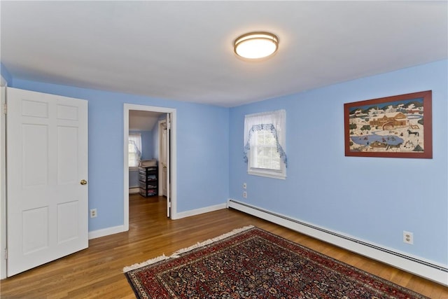 bedroom with baseboard heating, wood finished floors, and baseboards