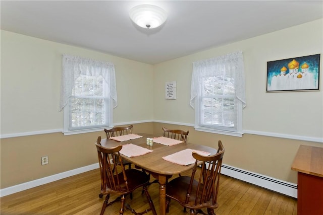 dining area featuring a baseboard heating unit, wood-type flooring, and baseboards