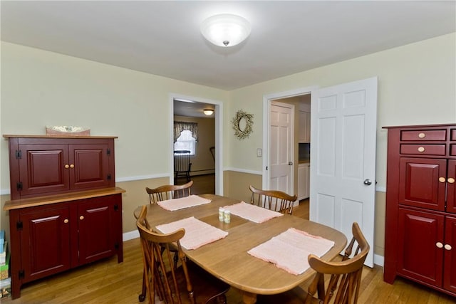 dining room with a baseboard heating unit, light wood-style flooring, and baseboards