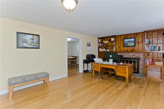 home office featuring a brick fireplace, light wood-style flooring, and baseboards