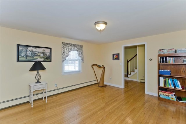 living area featuring a baseboard heating unit, light wood finished floors, stairs, and baseboards