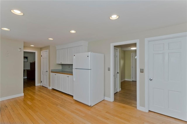 kitchen with baseboards, light wood-style flooring, freestanding refrigerator, white cabinetry, and recessed lighting