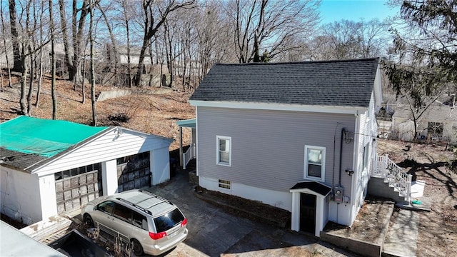 view of property exterior featuring a garage, an outdoor structure, and roof with shingles