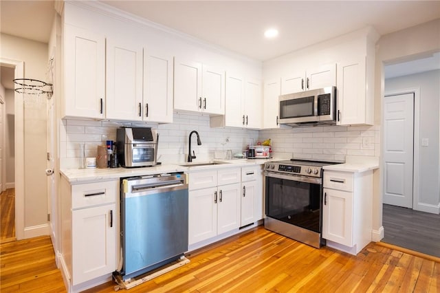 kitchen featuring light wood-style flooring, a sink, white cabinets, appliances with stainless steel finishes, and decorative backsplash