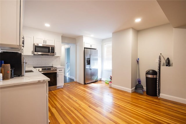 kitchen with appliances with stainless steel finishes, white cabinets, light wood-style floors, and decorative backsplash