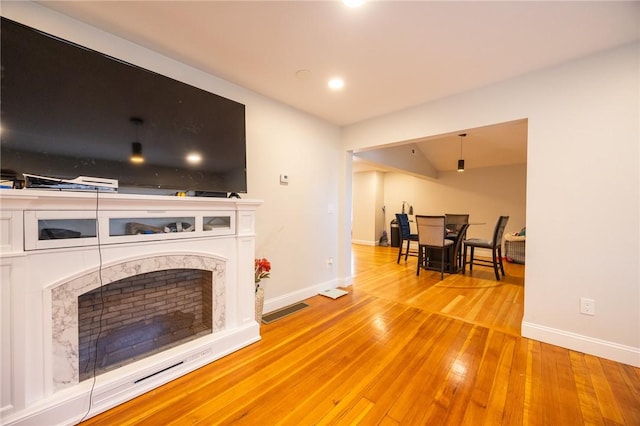 living room featuring light wood-style flooring, a premium fireplace, baseboards, and visible vents