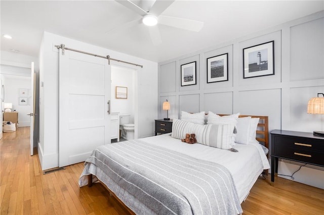 bedroom with ensuite bath, light wood-style floors, a barn door, and a decorative wall