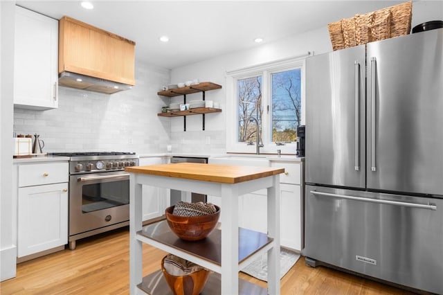 kitchen featuring light wood finished floors, wall chimney range hood, appliances with stainless steel finishes, and wood counters