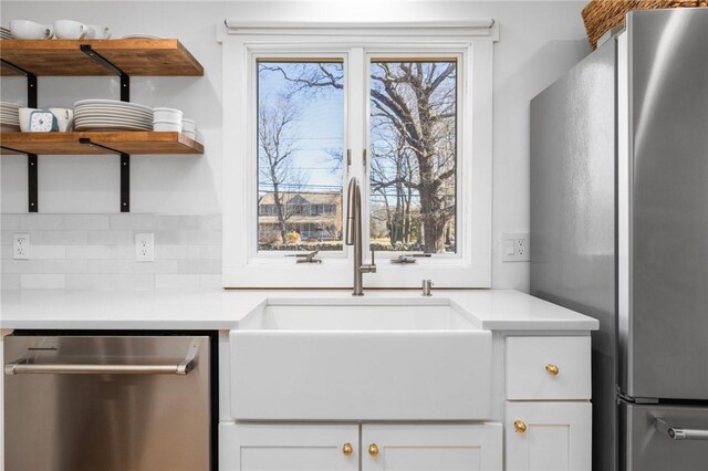 kitchen featuring open shelves, stainless steel appliances, light countertops, backsplash, and a sink