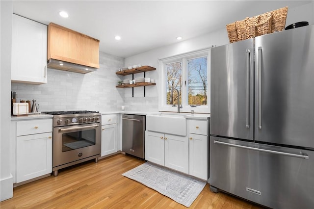 kitchen featuring stainless steel appliances, a sink, light countertops, light wood-type flooring, and decorative backsplash