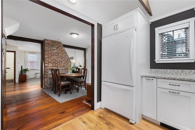 kitchen featuring light stone countertops, light wood-style floors, white cabinets, and freestanding refrigerator