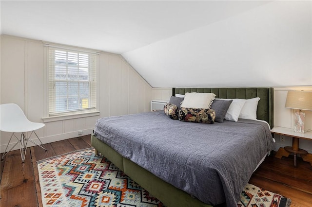 bedroom featuring lofted ceiling, a decorative wall, and hardwood / wood-style floors