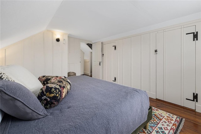 bedroom featuring vaulted ceiling, a decorative wall, and wood finished floors