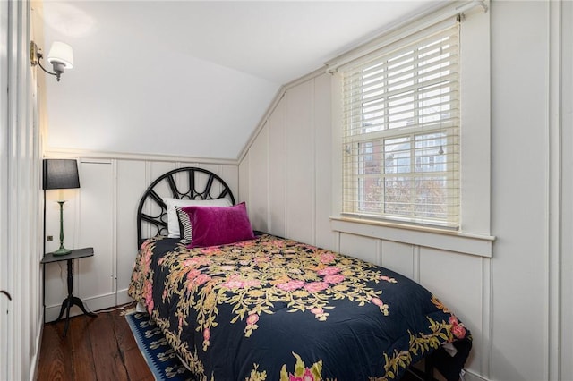 bedroom featuring lofted ceiling, a decorative wall, and wood finished floors