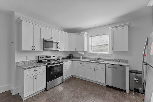 kitchen featuring appliances with stainless steel finishes, a sink, light stone counters, and white cabinets