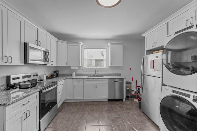 kitchen featuring appliances with stainless steel finishes, a sink, white cabinets, and stacked washer / drying machine