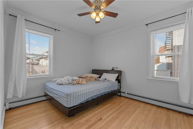 bedroom featuring light wood-style floors, crown molding, baseboard heating, and ceiling fan