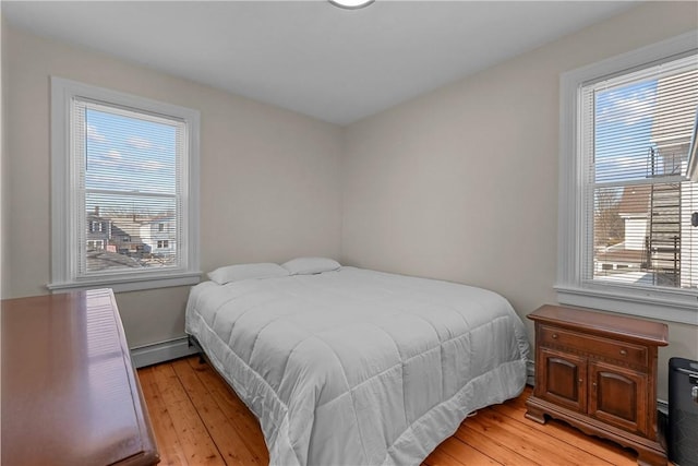 bedroom with light wood-style flooring, multiple windows, and a baseboard heating unit