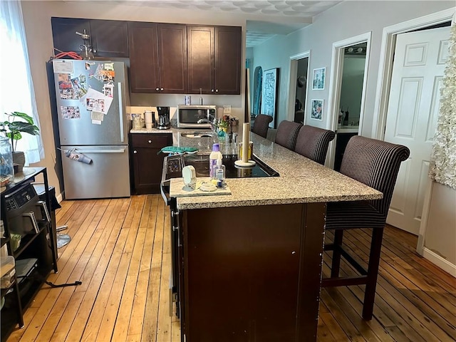 kitchen featuring dark brown cabinetry, light wood-style flooring, appliances with stainless steel finishes, and a kitchen breakfast bar