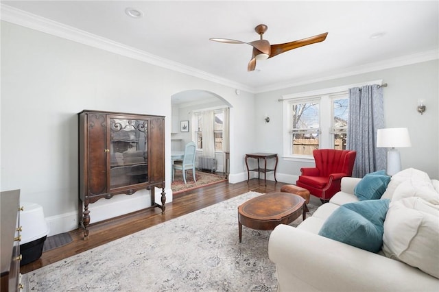 living room featuring arched walkways, wood finished floors, baseboards, radiator, and crown molding