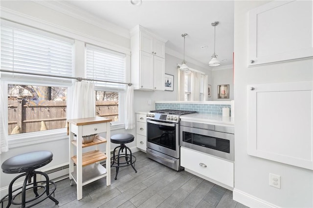 kitchen with hanging light fixtures, appliances with stainless steel finishes, light wood-style floors, ornamental molding, and white cabinets