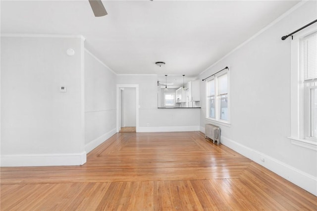 unfurnished living room featuring a ceiling fan, baseboards, ornamental molding, light wood finished floors, and radiator heating unit