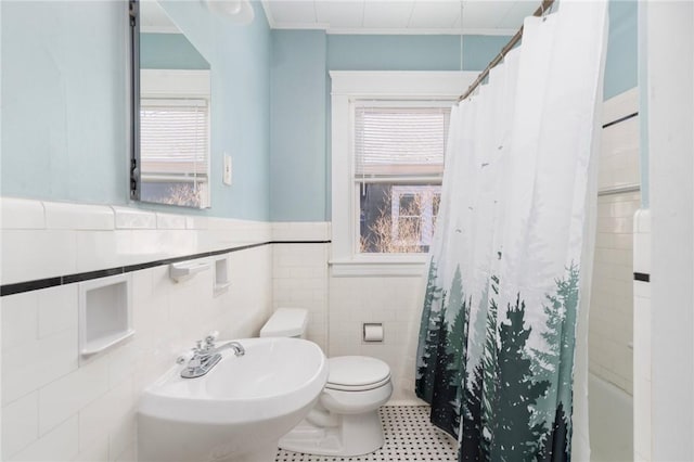 bathroom featuring a wainscoted wall, tile walls, toilet, ornamental molding, and a sink