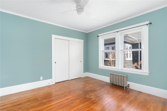 unfurnished bedroom featuring baseboards, radiator, ornamental molding, wood finished floors, and a closet