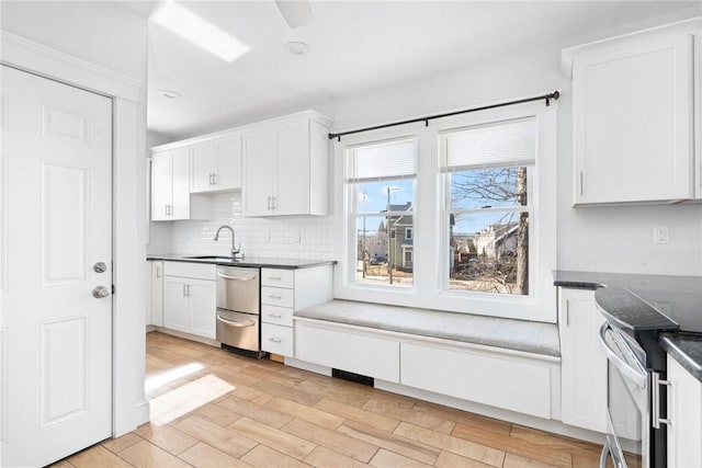 kitchen featuring light wood finished floors, white cabinets, dark countertops, a sink, and backsplash