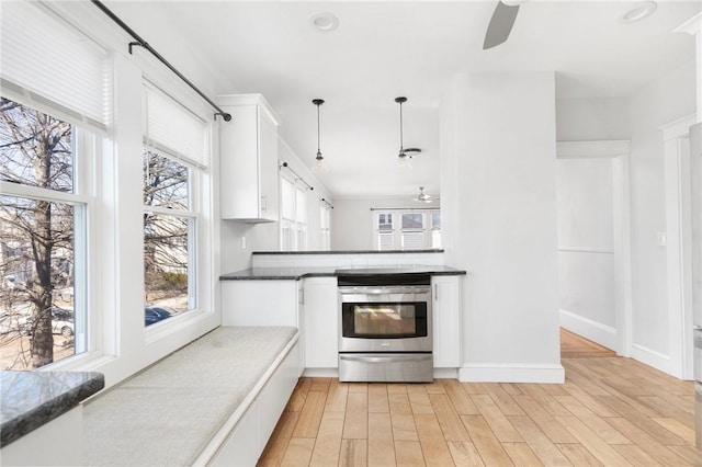 kitchen with light wood finished floors, white cabinets, dark countertops, stainless steel electric range oven, and ceiling fan