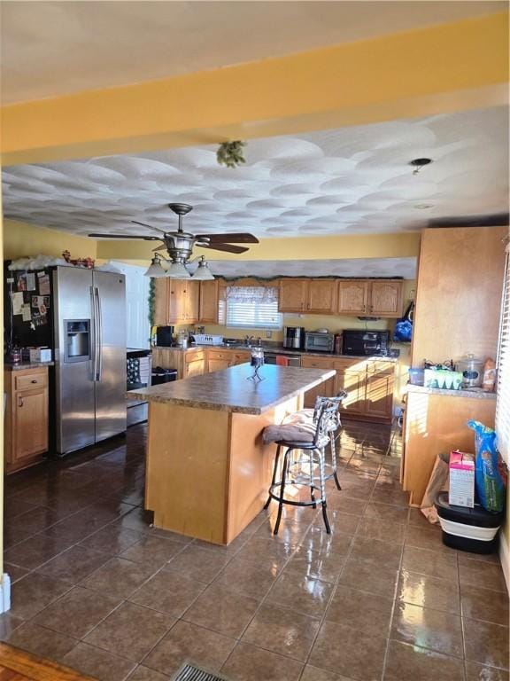 kitchen featuring a breakfast bar area, a kitchen island, ceiling fan, stainless steel fridge, and dark tile patterned floors