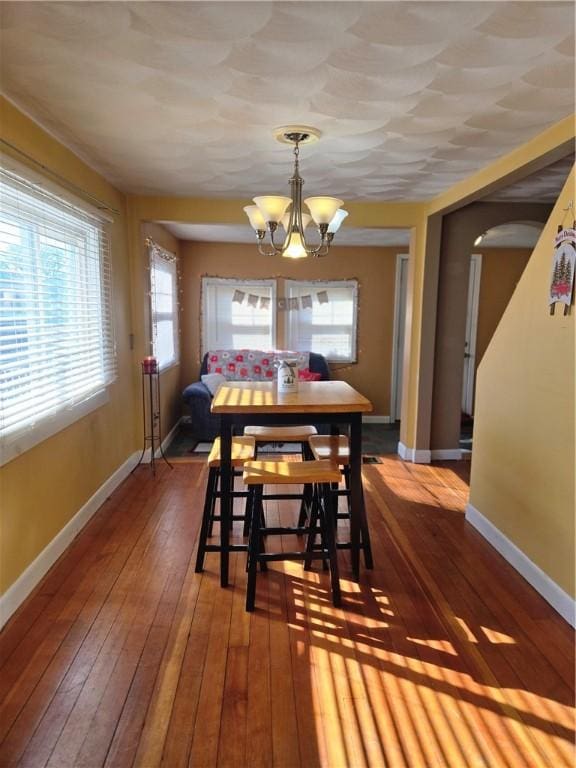 dining area featuring a notable chandelier, arched walkways, hardwood / wood-style flooring, and baseboards