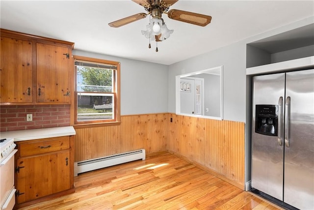 kitchen featuring a baseboard radiator, light wood-style flooring, wainscoting, brown cabinetry, and stainless steel fridge