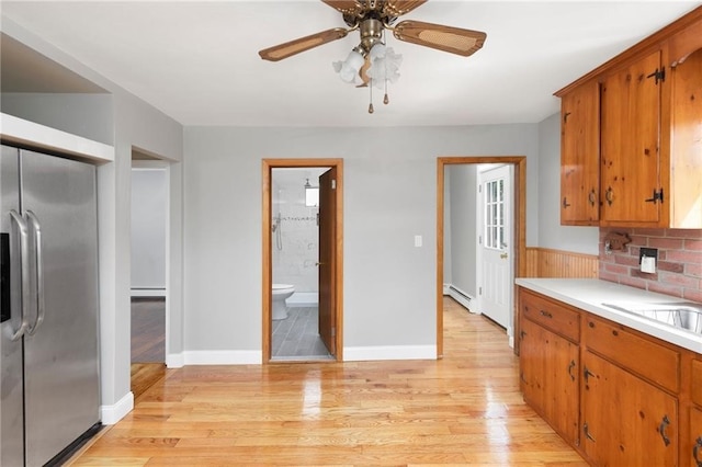 kitchen featuring ceiling fan, light wood-style floors, light countertops, brown cabinets, and stainless steel fridge