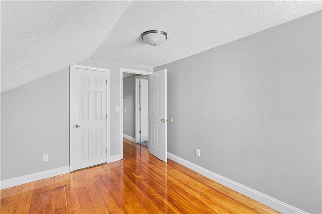 interior space with a textured ceiling, hardwood / wood-style floors, lofted ceiling, and baseboards