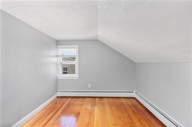 additional living space featuring a textured ceiling, a baseboard radiator, baseboards, vaulted ceiling, and light wood finished floors