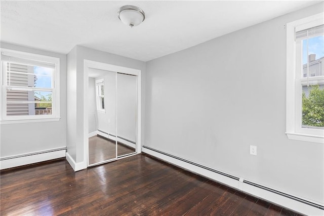 unfurnished bedroom featuring a baseboard heating unit, hardwood / wood-style floors, and multiple windows