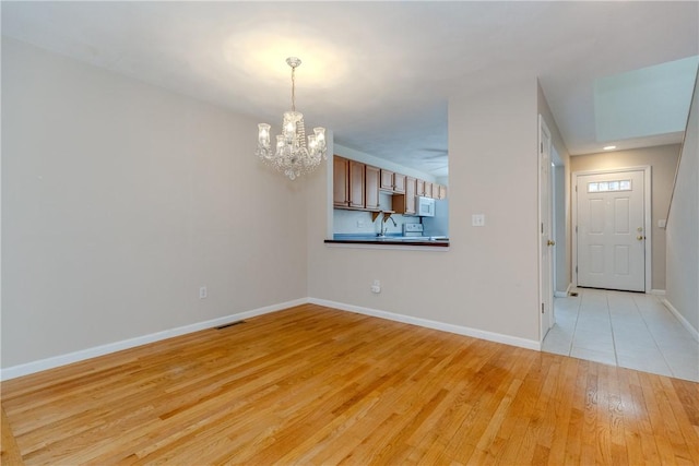 empty room with light wood finished floors, an inviting chandelier, visible vents, and baseboards