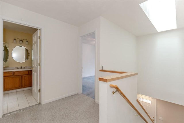 hall with a skylight, baseboards, light colored carpet, an upstairs landing, and a sink