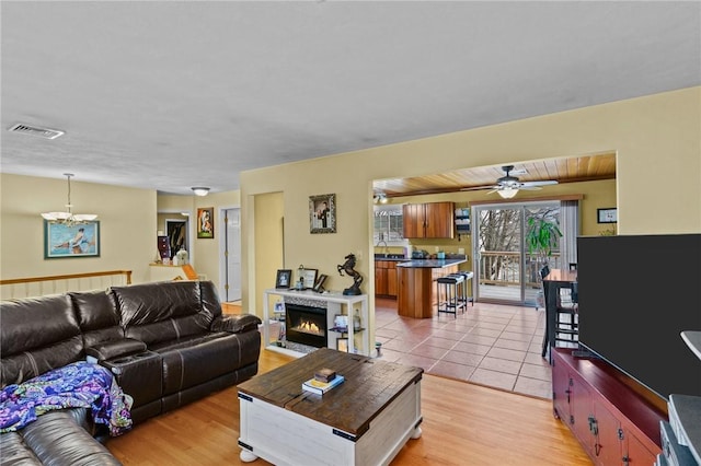 living room featuring light wood-style floors, a lit fireplace, visible vents, and a notable chandelier