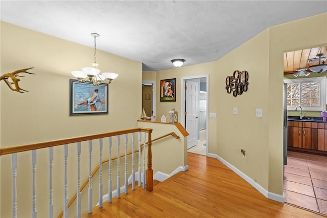 hall featuring baseboards, light wood-style flooring, a notable chandelier, an upstairs landing, and a sink