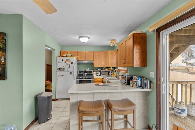 kitchen with appliances with stainless steel finishes, a peninsula, light countertops, a kitchen bar, and light tile patterned flooring