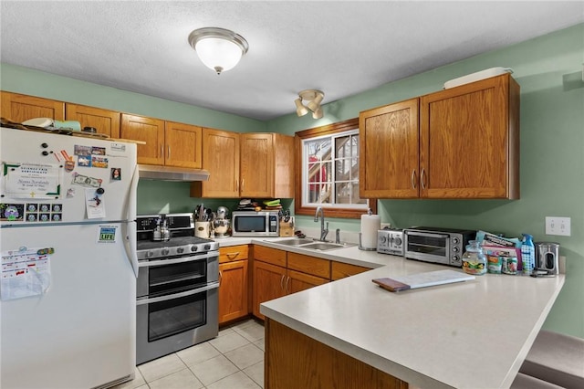 kitchen featuring appliances with stainless steel finishes, a peninsula, light countertops, under cabinet range hood, and a sink